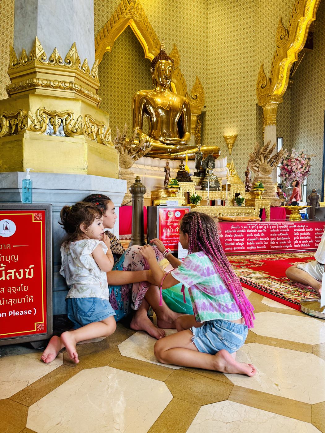 Three girls sitting on the marble floor in front of the golden Buddha at Wat Traimit