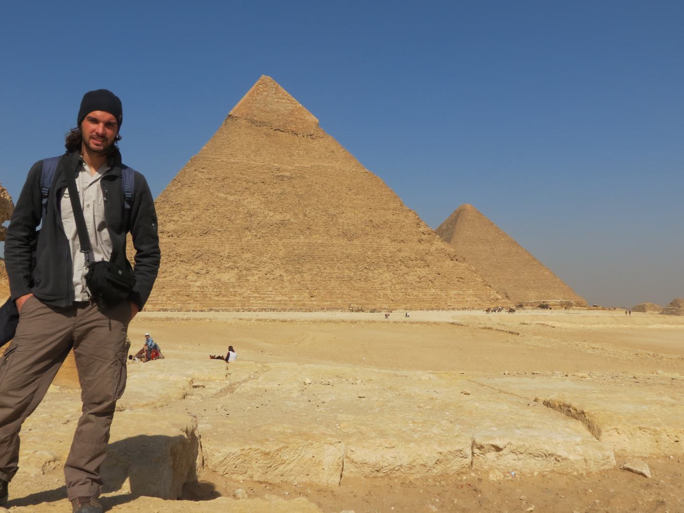 Young Ismael with long hair and a beanie in front of the Giza pyramids