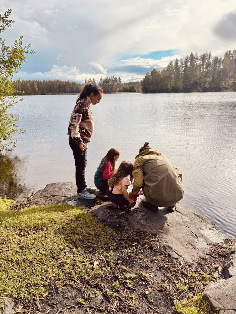 Family crouched on a rock at a lake shore looking into the water