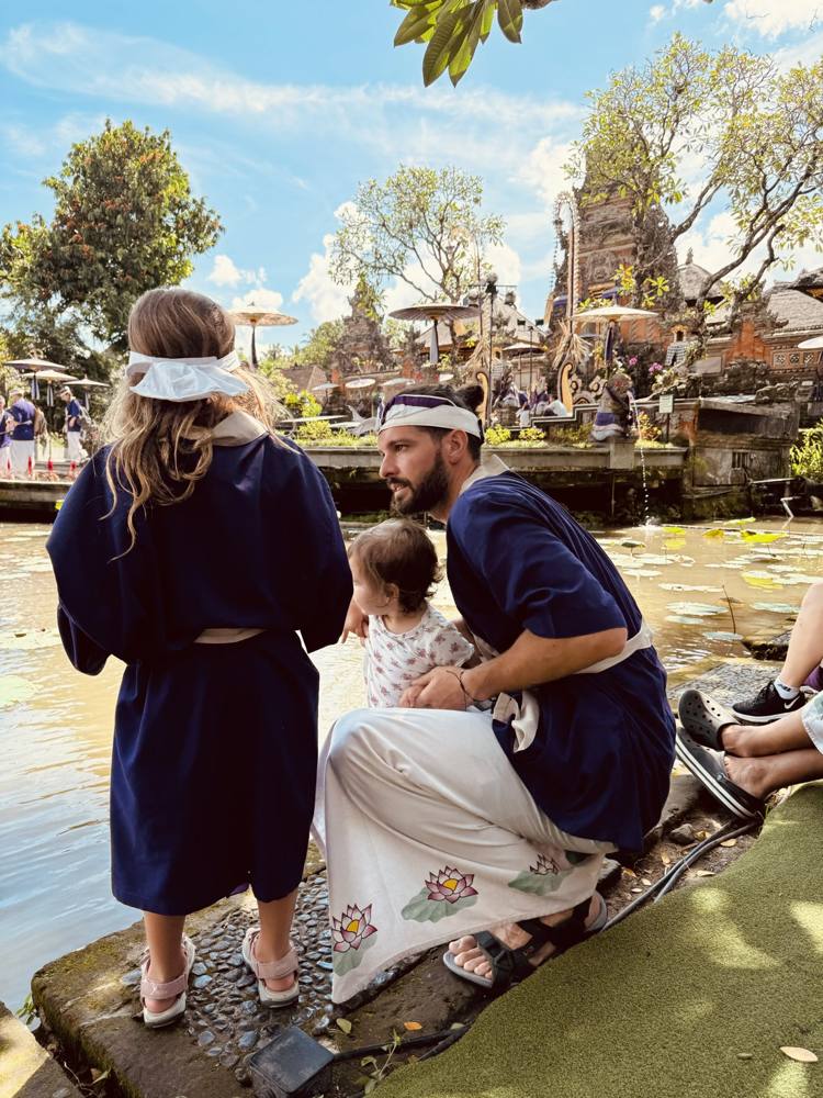 Ismael and his daughters in blue robes beside a lily pond at a water temple in Ubud