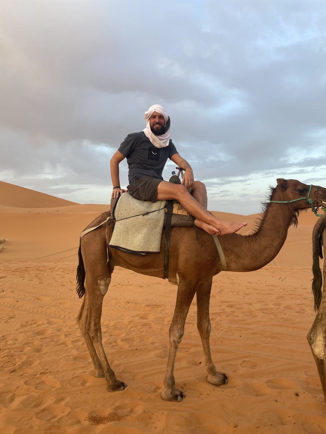 Ismael in a head wrap sitting on a camel in the Sahara dunes