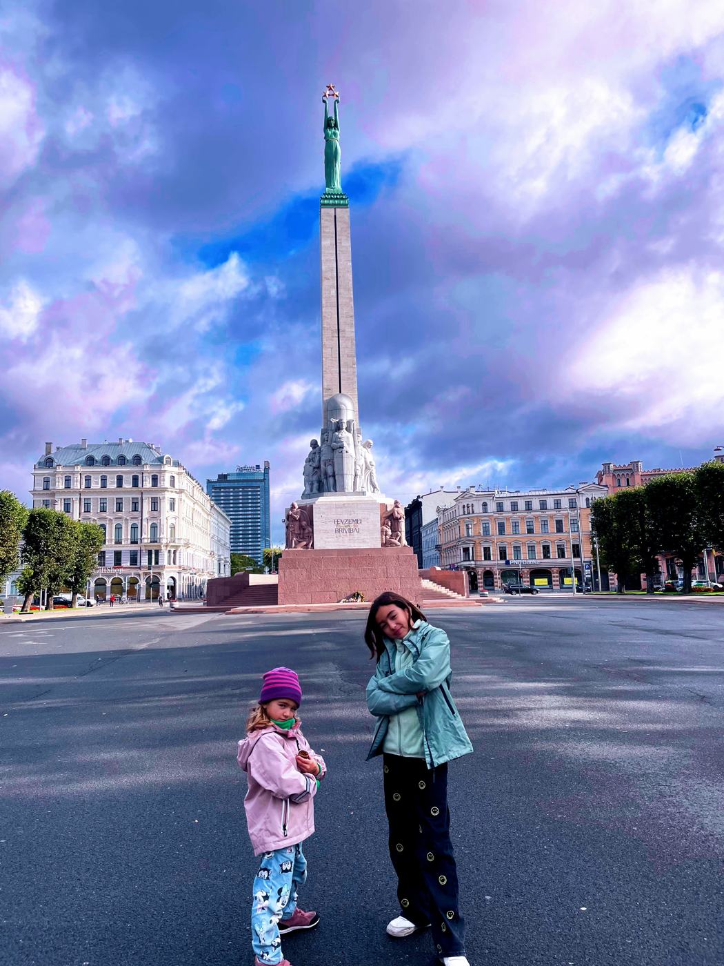 Two girls posing in front of the Freedom Monument under a dramatic purple sky