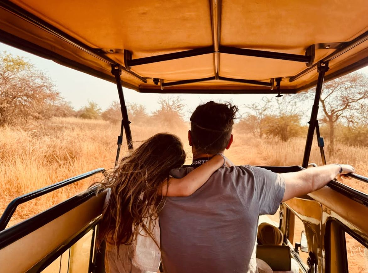 Father and daughter seen from behind in an open safari vehicle, looking over golden savanna
