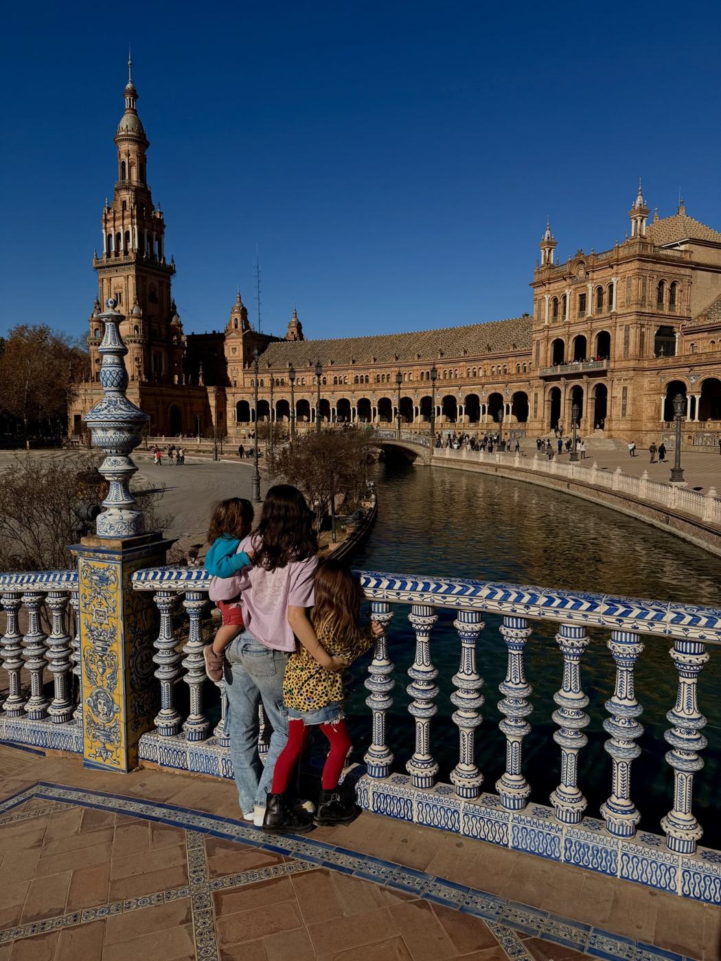 Family looking over a tiled bridge railing at Plaza de España, Seville