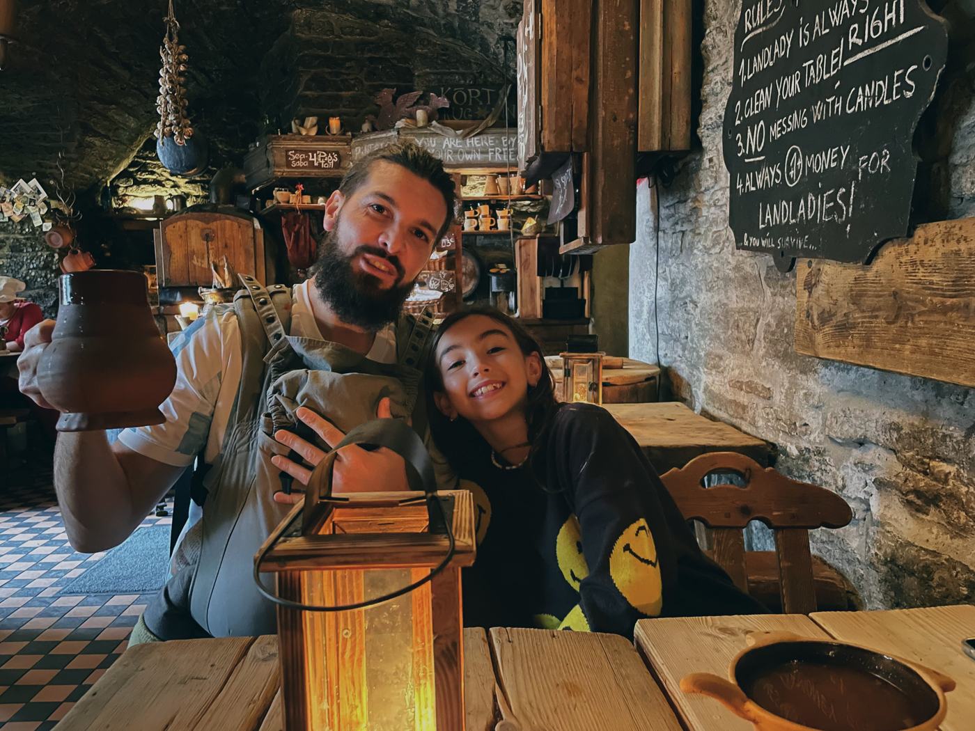 Ismael raising a clay mug and his daughter leaning on him in a candlelit medieval tavern